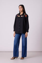 Model wearing a black button-down with embroidered flowers and denim.